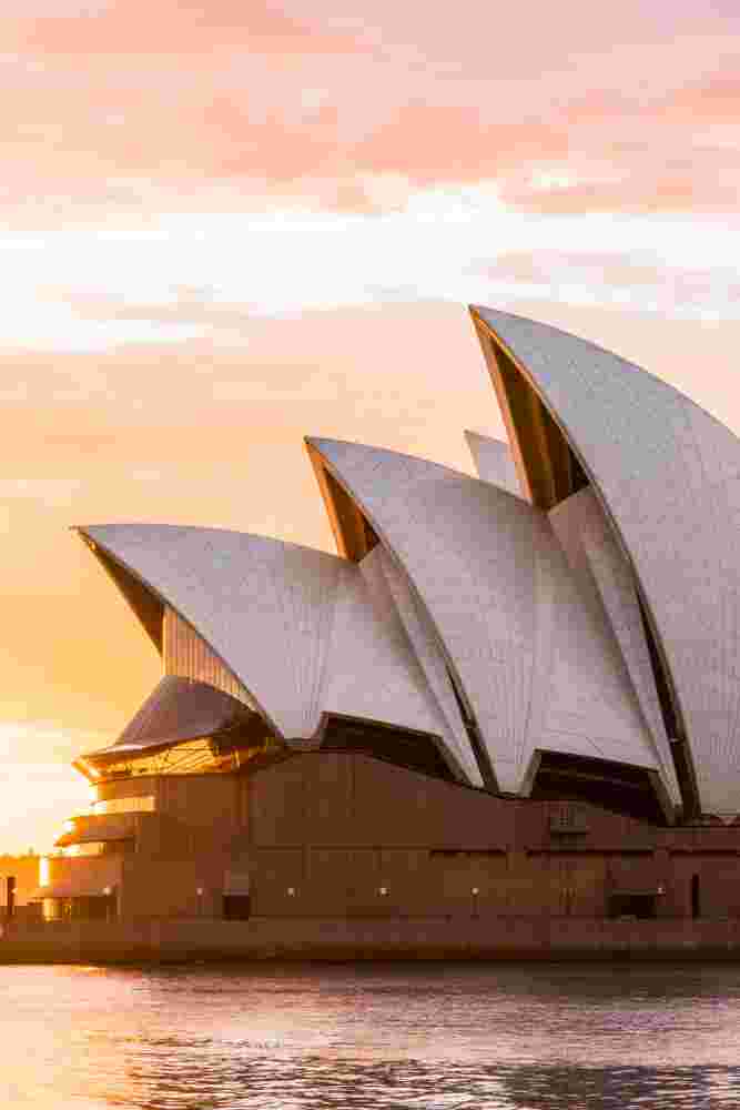 Sydney Opera House with White Sail-like Roofs at Sunset over Sydney Harbour, Water in the Foreground.